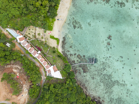 Aerial view of the Cottage Legon Waru nestled amidst lush greenery where the turquoise waters meet the sandy shore, Karimunjawa, Central Java, Indonesia.