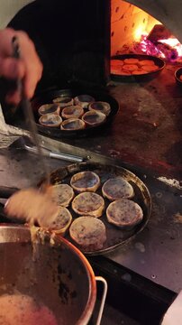 Traditional Udmurt perepechi being prepared in a wood fired oven. Burning fire in the background while mushroom filling is poured into small dough cups before baking. Authentic rustic cooking process
