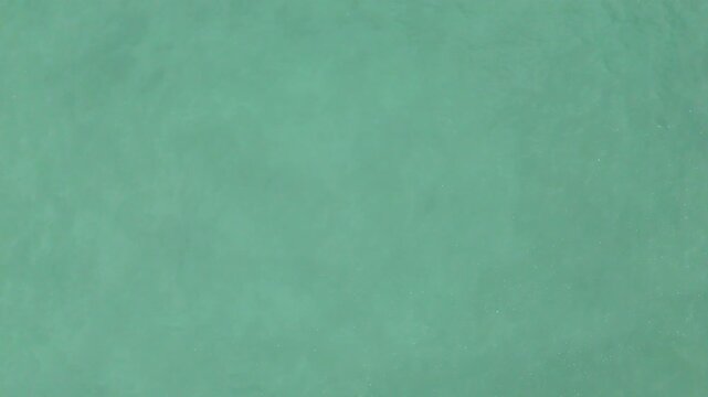 Aerial slow motion view of turquoise water surface with subtle ripples and light reflections over open sea