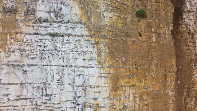Slow aerial pan of cliff face showing streaking erosion and crumbling rock on coastal bluff in overcast daylight