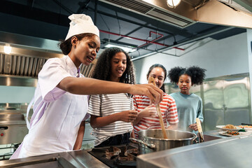 Professional chef instructor stirring soup while teaching teenager cooking students in commercial kitchen, culinary training and hospitality education concept