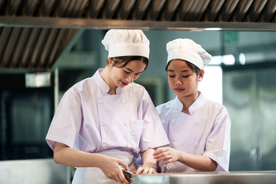 Teenage chef students wearing professional chef uniform learning cooking techniques in culinary school kitchen, hospitality education concept
