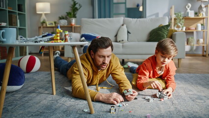 Dad child playing lego lying home floor. Boy building toy figure with father © stockbusters