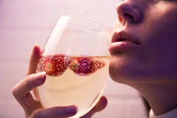 Close-up portrait of a woman sipping sparkling wine with strawberries floating in the glass, capturing a sensual, refreshing and intimate moment with soft light and elegant composition © splendens