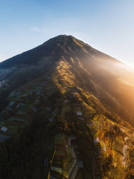 Aerial view of a towering mountain peak kissed by the warm glow of sunrise, casting long shadows across the terraced fields below, Nepal van Java, Jawa Tengah, Indonesia.