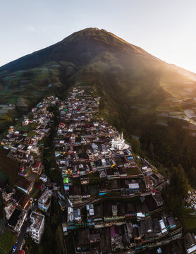Aerial view of a densely packed village cascading down the verdant slopes beneath a towering mountain peak, Nepal van Java, Jawa Tengah, Indonesia.
