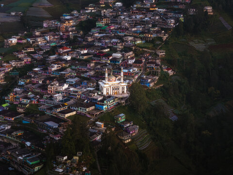 Aerial view of a mosque standing prominently amidst a densely packed town, nestled between verdant hills and terraced fields, Nepal van Java, Jawa Tengah, Indonesia.