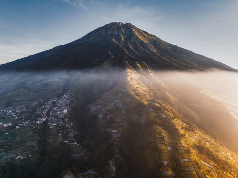 Aerial view of a majestic mountain peak rising above a sea of clouds, casting shadows on the lush green terraces below, Nepal van Java, Jawa Tengah, Indonesia.