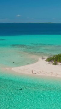 Capturing the beauty of the maldives from above, this aerial drone image shows a turquoise lagoon with a woman strolling on a white sand beach