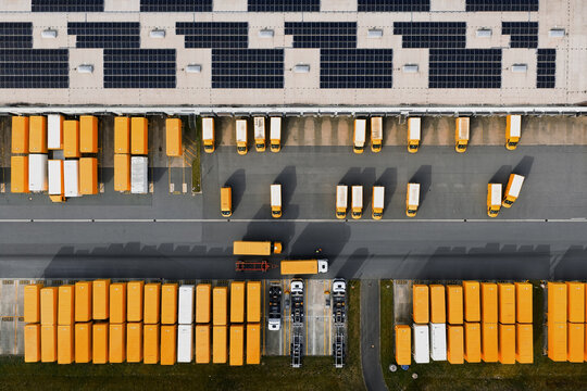 Aerial view of yellow and white trucks lined up neatly at the warehouse with solar panels on the roof, North Rhine-Westphalia, Germany.