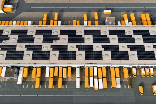 Aerial view of bright yellow delivery trucks contrasting against the dark solar panels atop a distribution center, North Rhine-Westphalia, Germany.