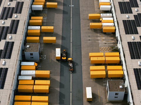 Aerial view of a logistics hub with rows of yellow container trailers parked neatly between buildings equipped with solar panels, North Rhine-Westphalia, Germany.