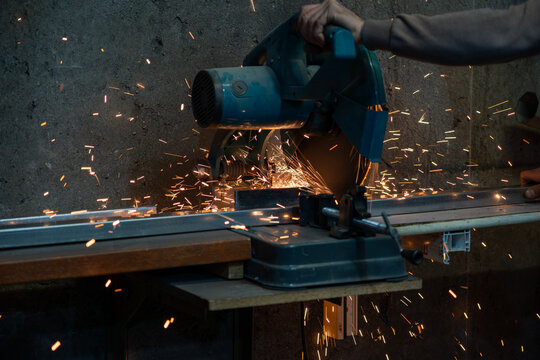 Cutting steel profile with electric miter saw and flying sparks in industrial metal fabrication environment.