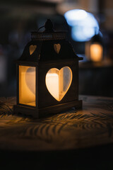Romantic heart-shaped lantern with a glowing candle on a table at night with soft bokeh.