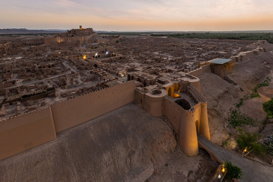Aerial view of the ancient Arg-e Bam citadel's weathered walls standing resilient against the horizon's soft glow, a testament to time's passage, Bam, Kerman Province, Iran.