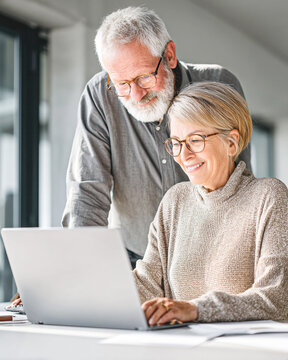 An elderly couple happily working together on a laptop in a bright, modern home office setting.
