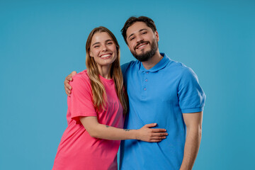 Naklejka premium Happy young couple smiling at camera standing together on blue studio background