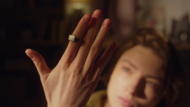 Rack focus shot of frustrated young adult woman sitting on bed looking at ring on finger then holding head with overwhelmed expression while going through emotional crisis