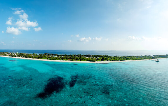 Aerial view of the turquoise sea swirling around the lush, green island, where the white sandy beach kisses the darker trees, Vashafaru, Haa Alif, Malediven.