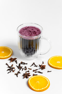 Red hot mulled wine for a cozy cold evening to warm up in a transparent double wall cup or mug on white background, star anise and cloves spices around, fresh citrus orange wheels 