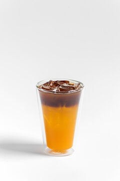 Refreshing bumble orange citrus juice and black coffee espresso drink with ice in a transparent double wall glass on white background 