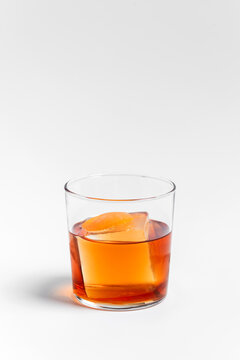 Old fashioned alcoholic cocktail in a transparent rocks glass with a big ice cube and orange peel garnish on white background 