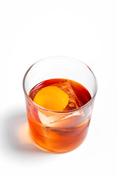 Old fashioned alcoholic cocktail in a transparent rocks glass with a big ice cube and orange peel garnish on white background 
