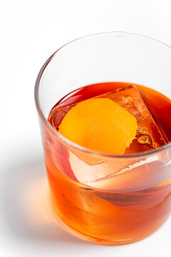 Old fashioned alcoholic cocktail in a transparent rocks glass with a big ice cube and orange peel garnish on white background 