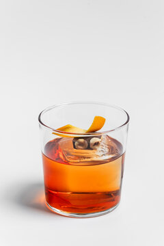 Old fashioned alcoholic cocktail in rocks glass with ice cube, orange twist and a piece of chocolate with hazelnut garnish on white background 