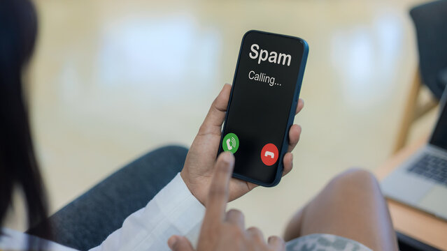 Spam call notification on smartphone screen alert. Cyber scam and telemarketing fraud protection concept. Mobile security and identification. Woman holding phone with unwanted spam call display.