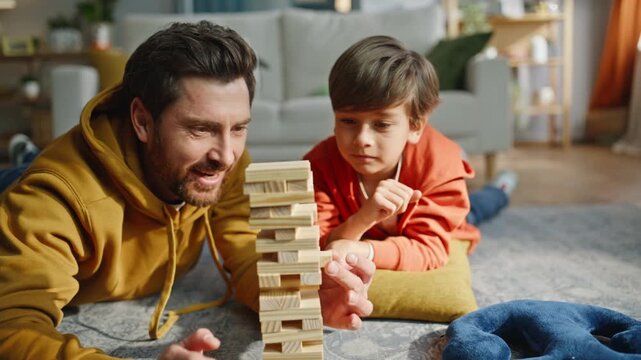 Father son playing jenga lying floor closeup. Smiling man playful boy game