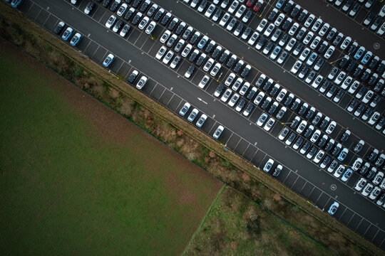 Aerial view of orderly rows of parked cars contrast with the adjacent earthy fields, a testament to industrial precision, Stone, England, United Kingdom.