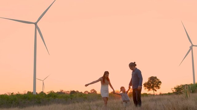 Family with son walking on field on wind farm. Happy Family and son playing at the Wind turbines generating electricity. Family time together.