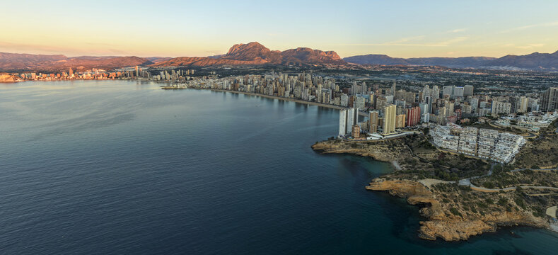 Aerial view of towering buildings lining the coast where the deep blue sea meets the shore at sunrise, Benidorm, Valencian Community, Spain.