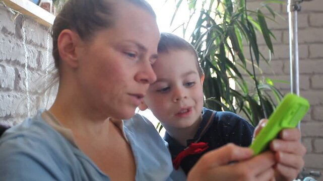 Mother and son, a small child, are sitting on the sofa looking at the phone