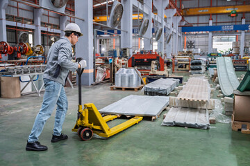Fototapeta premium Industrial worker using a pallet jack to transport materials inside a modern factory. Concept of manufacturing, logistics, productivity, and warehouse management in industrial operations.
