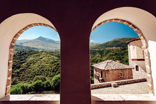 View of stone buildings framed by arched windows, revealing verdant hills against a clear sky, creating a captivating contrast of rustic charm and natural beauty, Mavrove, North Macedonia.
