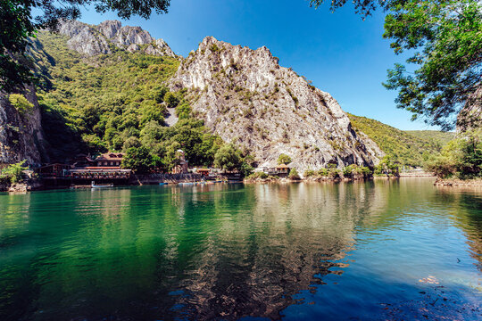 View of shimmering emerald waters reflect the craggy rock faces and lush green forests under a vibrant blue sky, casting a spellbinding scene, Skopje, North Macedonia.