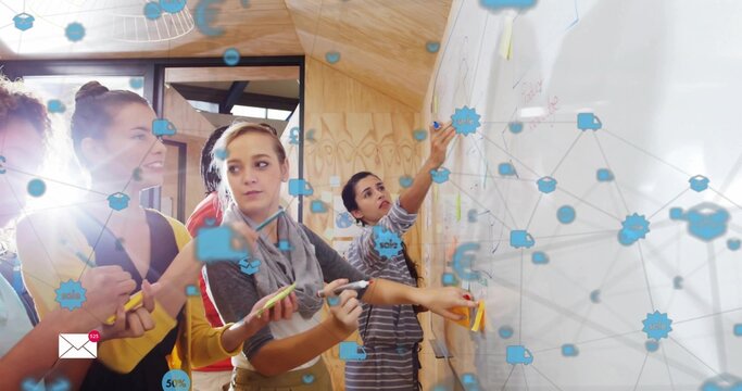 Designing team wearing casual attire placing sticky notes on whiteboard in studio with blue overlay