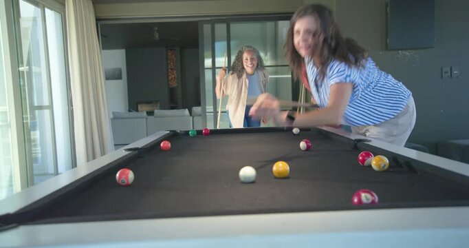 Diverse female friends responding to cheers, taking shots on black-felt pool table in game room