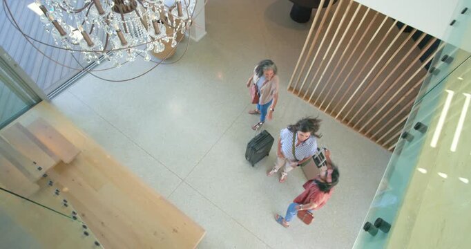 Diverse trio with senior Latina and two others arriving hotel lobby pulling bags near chandelier