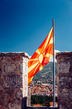View of the North Macedonia flag waving proudly against a clear blue sky, framed by weathered stone, overlooking the town below, Ohrid, Municipality of Ohrid, North Macedonia.