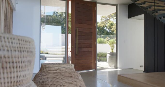 Two women entering foyer with pivot door opening behind, walking in from sunny patio carrying bags