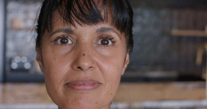 First frames showing mature woman opening eyes and smiling, responding to camera at kitchen shelf