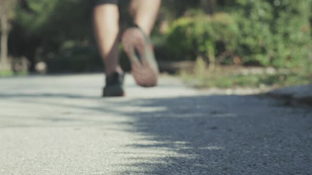 Out of focus shot of a man walking on a path in a park environment. Cinematic shallow depth of field creating mystery, surveillance and suspense concept. Authentic outdoor footage, real environment, n