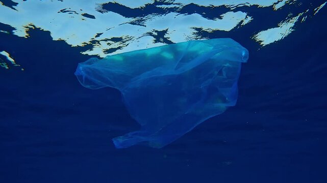 Bottom view on used old disposable transparent blue plastic bag swims in sunrays below water surface, Slow motion, Underwater shot on plastic pollution of the Ocean
