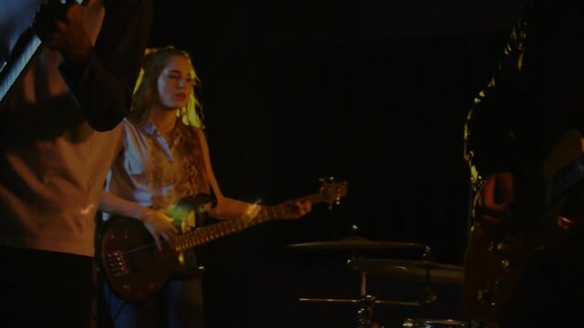 Camera pulling back lead singer playing guitar into vintage mic, band playing music, lights flaring