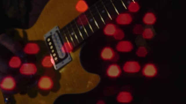 Camera shifting, guitarist's hands plucking strings for recording, red hex bokeh overlaying guitar