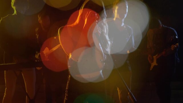 Singer leaning into mic, camera focus shifting, bokeh revealing guitars and keyboard in music show