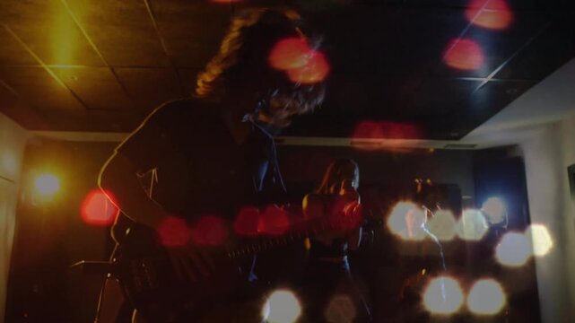 Camera pullback revealing guitarist moving and vocalist singing in music session with hex bokeh mic